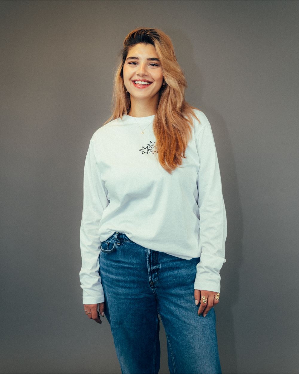 Weiße Longsleeve-Shirt-Ansicht von vorn. Auf der linken Brustseite befindet sich ein schwarzer Frontprint aus drei ineinander verschlungenen Sternformen, die gemeinsam ein Herzmotiv bilden. Das Shirt hat einen klassischen Rundhalsausschnitt und besteht aus weichem Baumwollstoff mit lockerer Passform.