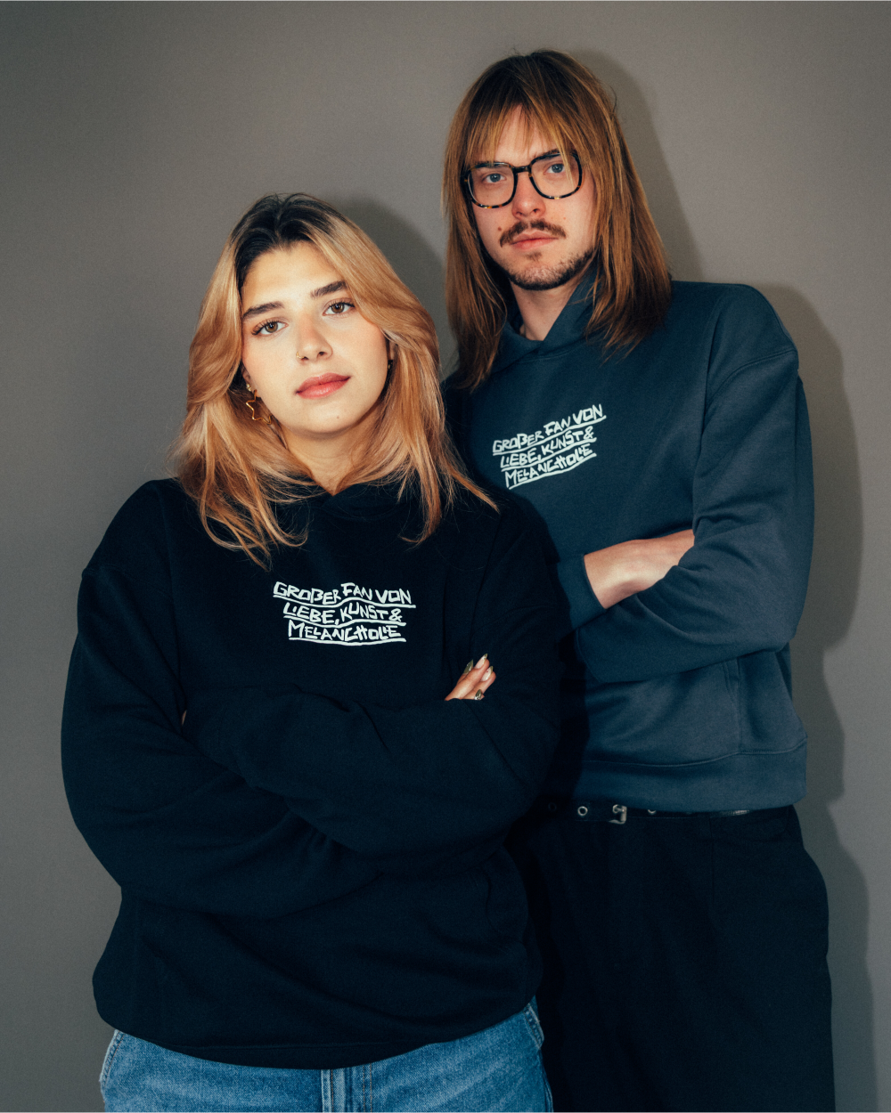 Schwarzer Hoodie aus Baumwollmischung mit weißem Frontprint in handschriftlicher Schriftart. Der Text lautet: „GRÖßER FAN VON LIEBE, KÜNSTEN & MELANCHOLIE“. Das Modell hat eine Kapuze ohne Kordelzug, eine große Kängurutasche sowie elastische Rippbündchen an Ärmeln und Saum. Locker geschnitten für einen lässigen Look.