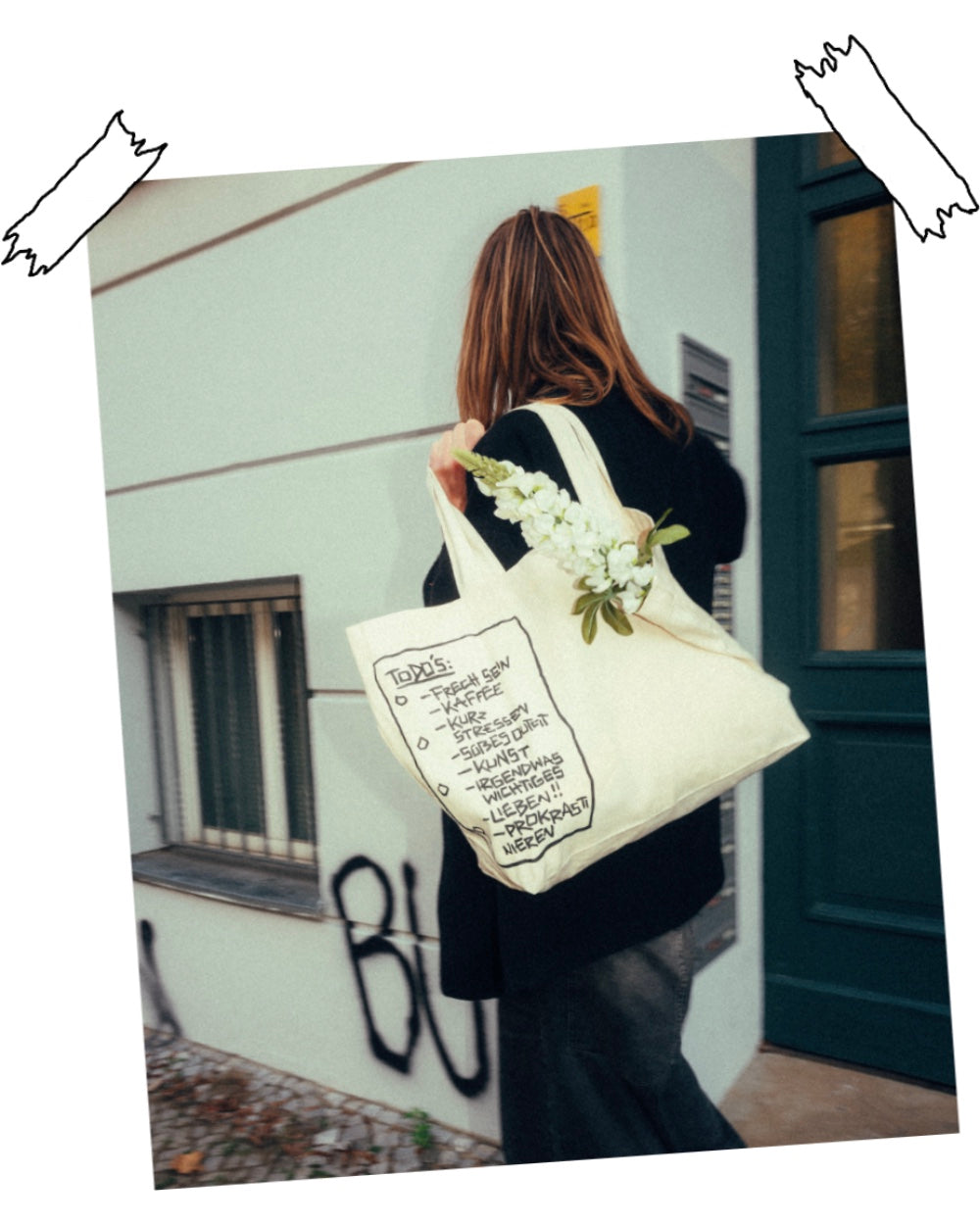 Beiger Stoff-Shopper aus robustem Canvas mit schwarzem Print einer handgezeichneten To-do-Liste. Darauf stehen humorvolle Punkte wie „FRECH SEIN“, „KAFFEE“, „KURZ STRESSEN“, „SÜßES OUTFIT“, „KUNST“, „IRGENDWAS WICHTIGES“, „LIEBEN!!“ und „PROKRASTINIEREN“. Die Tasche wird über der Schulter getragen, mit weißen Blumen befüllt. Lässiger, alltagstauglicher Shopper mit kreativem Illustrationsdruck.